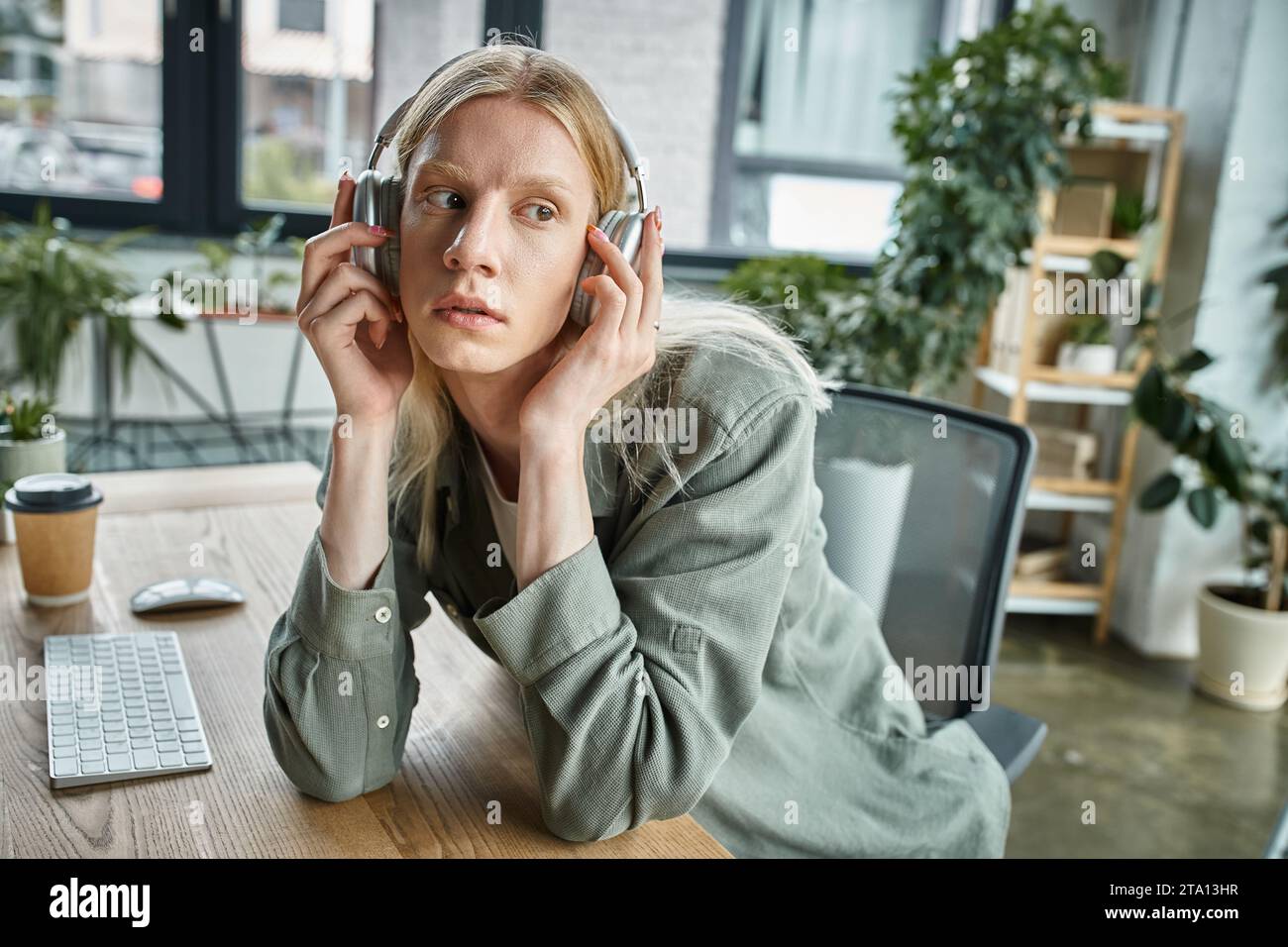 appealing androgynous person sitting at desk with headphones and looking away, business concept Stock Photo