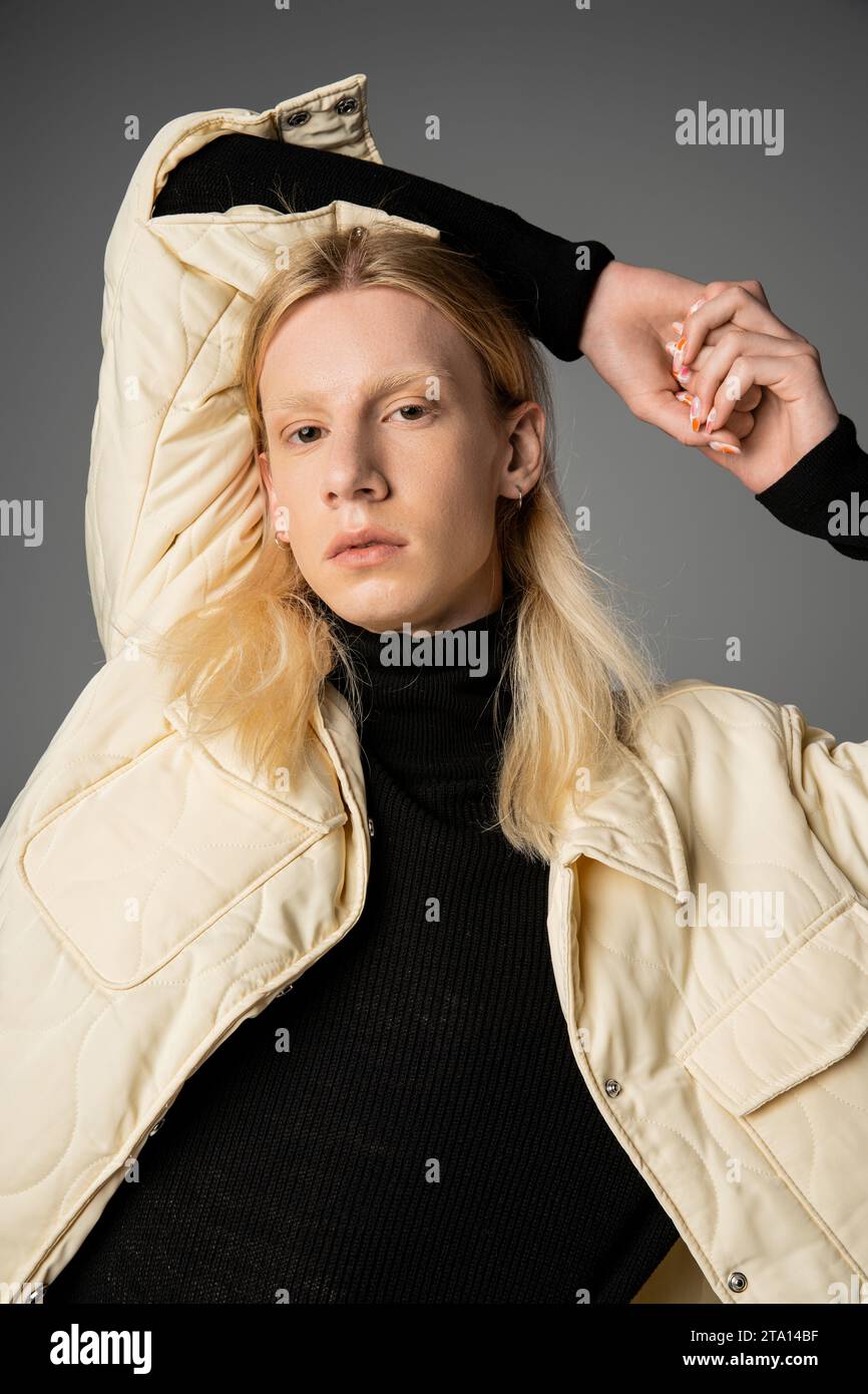 attractive androgynous person in winter stylish jacket posing on gray backdrop with arms above head Stock Photo