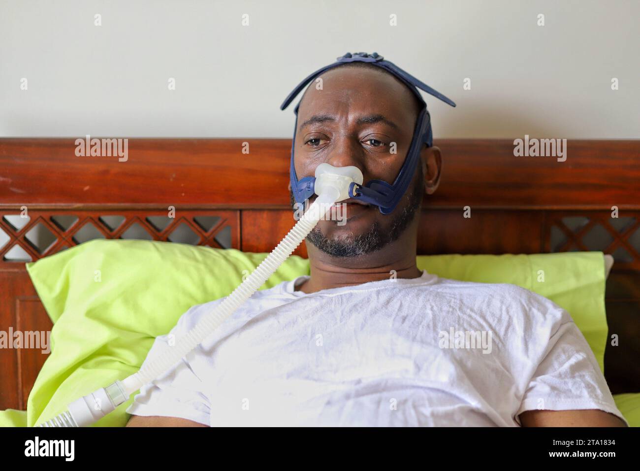 An AfricanAmerican man wearing cpap mask while laying in bed Stock
