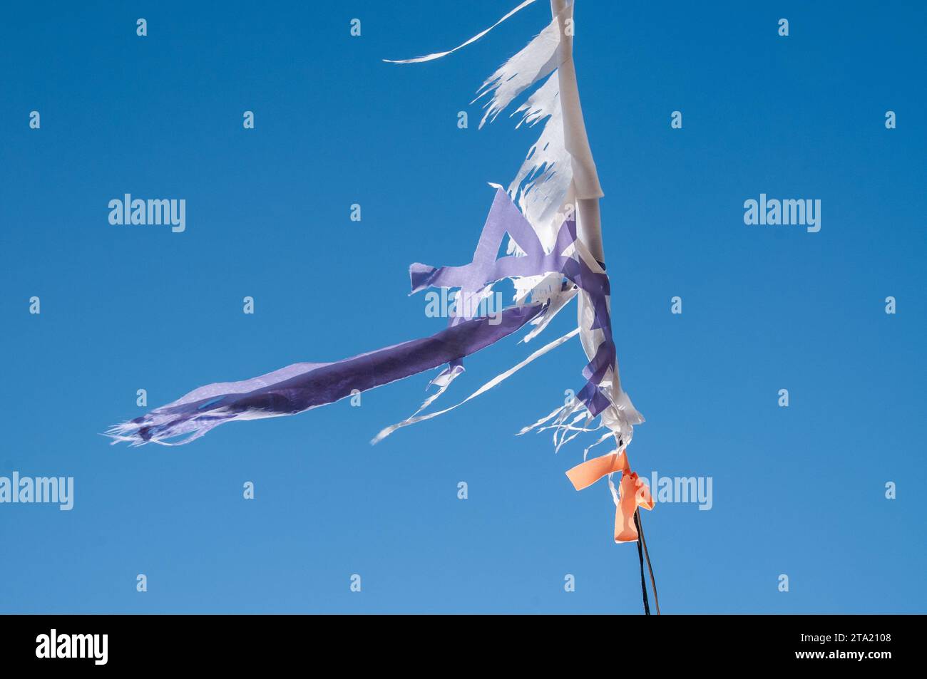 Worn and weathered, torn and tattered remnants of an Israeli flag flutters in the breeze on sunny day. Stock Photo