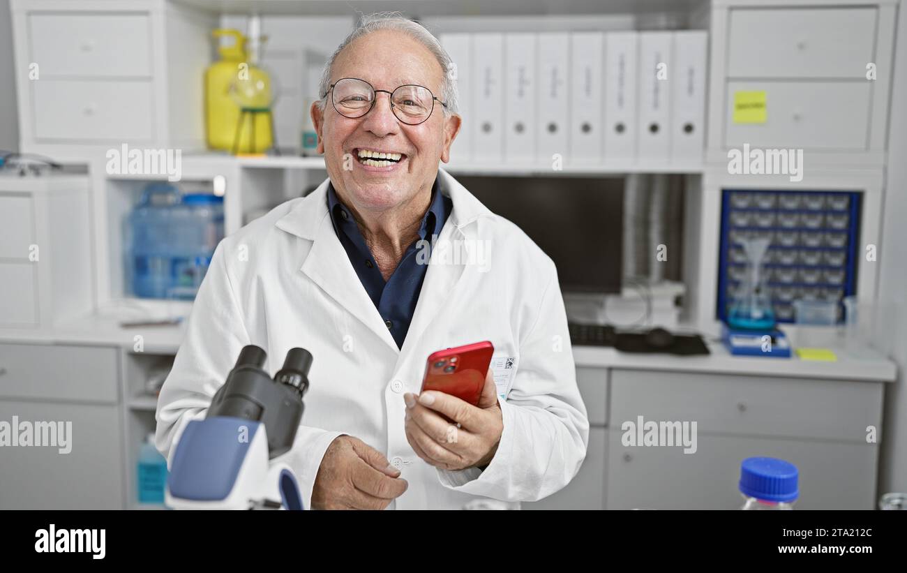 Senior man scientist smiling confident using smartphone at laboratory Stock Photo