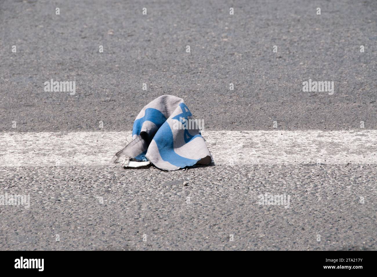A small, dirty, blue and white flag of the State of Israel lies on asphalt pavement after falling from a car. Stock Photo