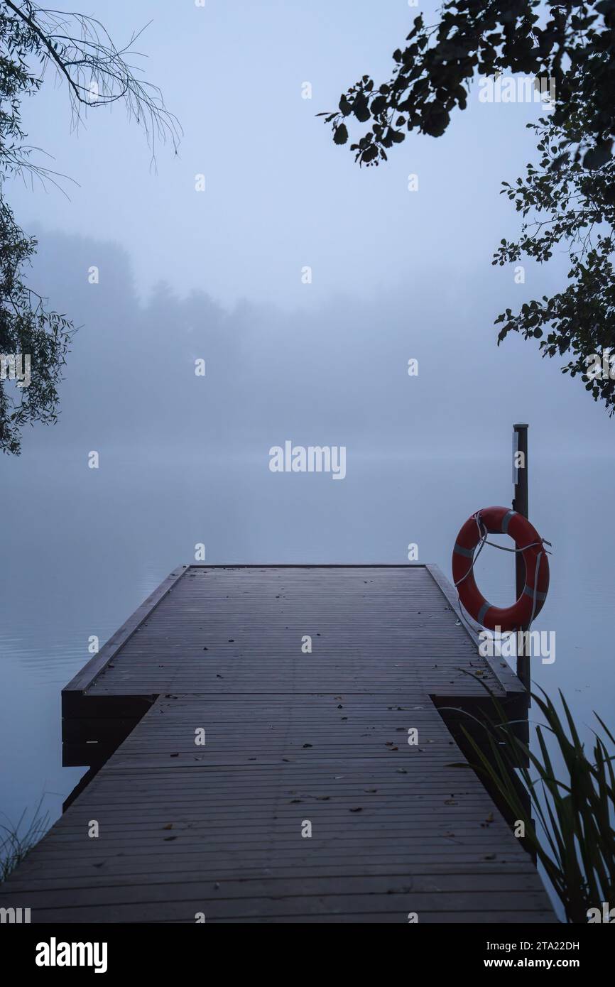 Wooden pier in the blue morning mist, with a life preserver ring hanging on a pole Stock Photo