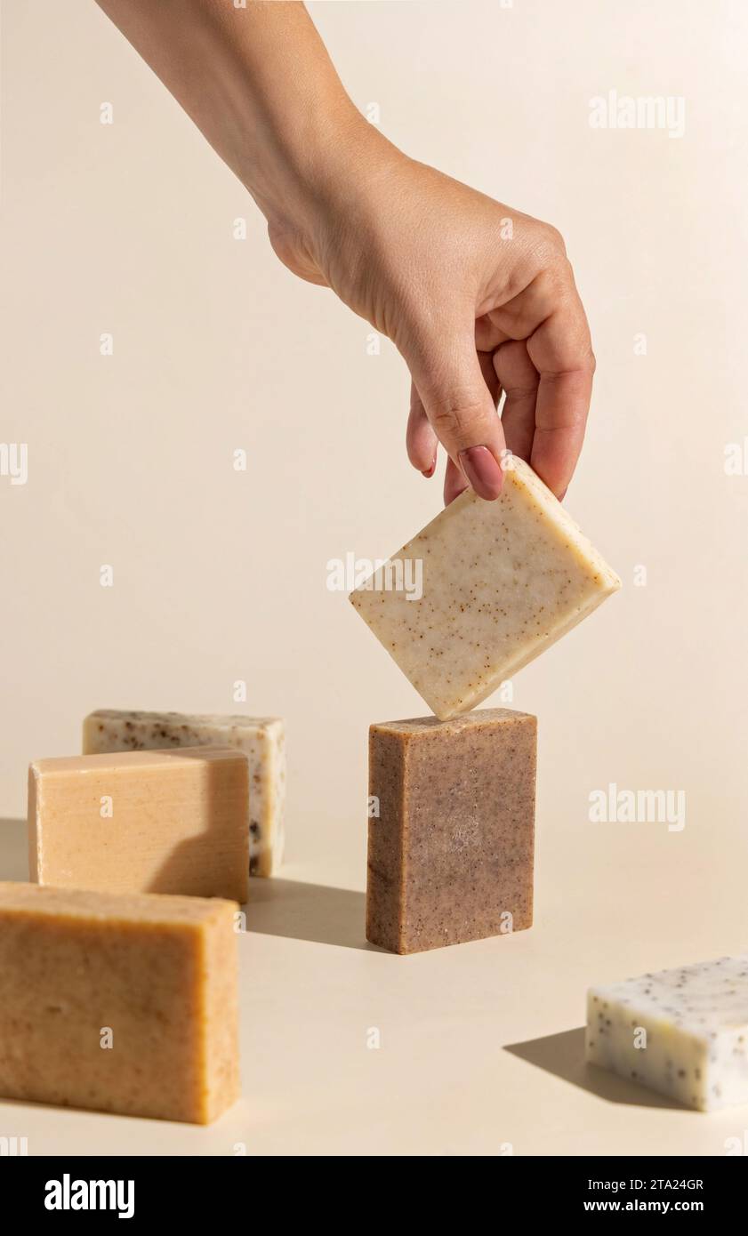 Hand keeps natural beige and brown soap bars on light beige, close up, hard shadows. Hygiene products for Spa and skin care. Using organic handmade so Stock Photo