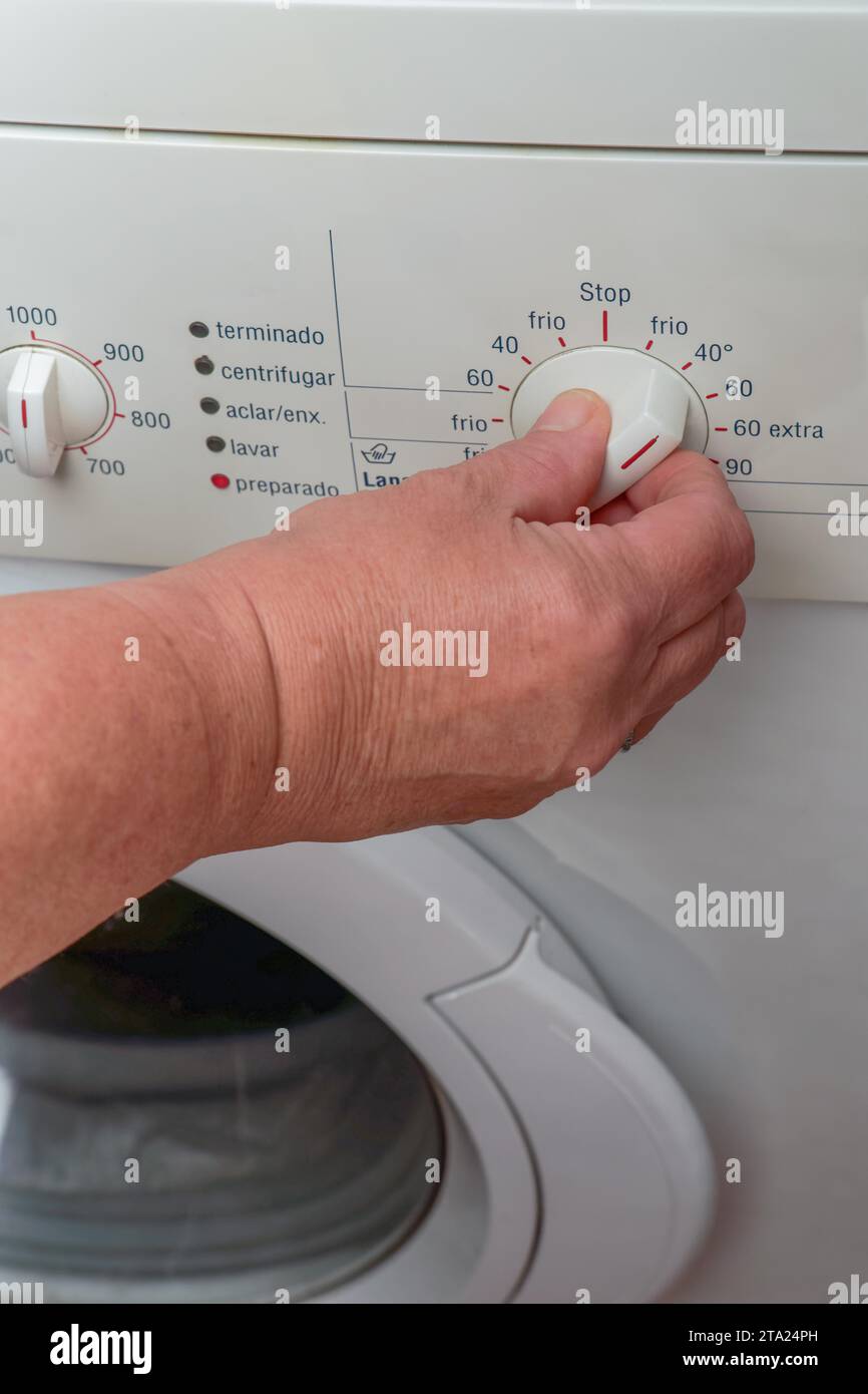 Woman hand choosing program on automatic washing machine for laundry at home. Turning knob on control panel Stock Photo