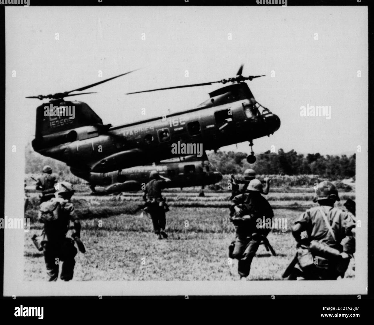 Two CH-46 helicopters hover above a jungle clearing during the Vietnam War. The helicopters, robustly constructed, were widely used by the American military during the conflict for troop and supply transportation. This photograph captures the operational deployment of these aircraft and provides a glimpse into the chaotic environment of Vietnam. Stock Photo