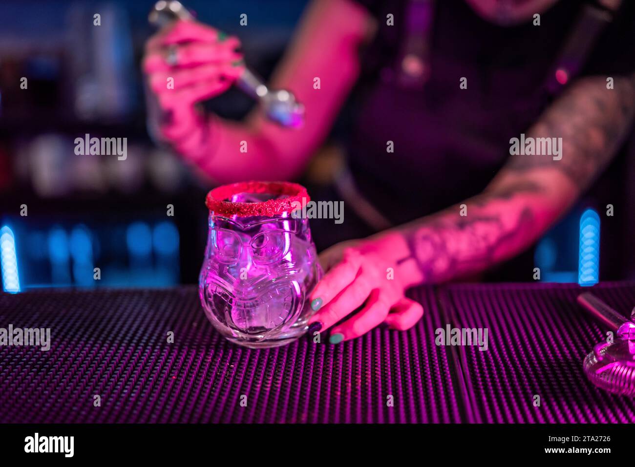 Close-up of a bartender preparing a margarita cocktail adding ice in the counter of a bar with neon lights Stock Photo