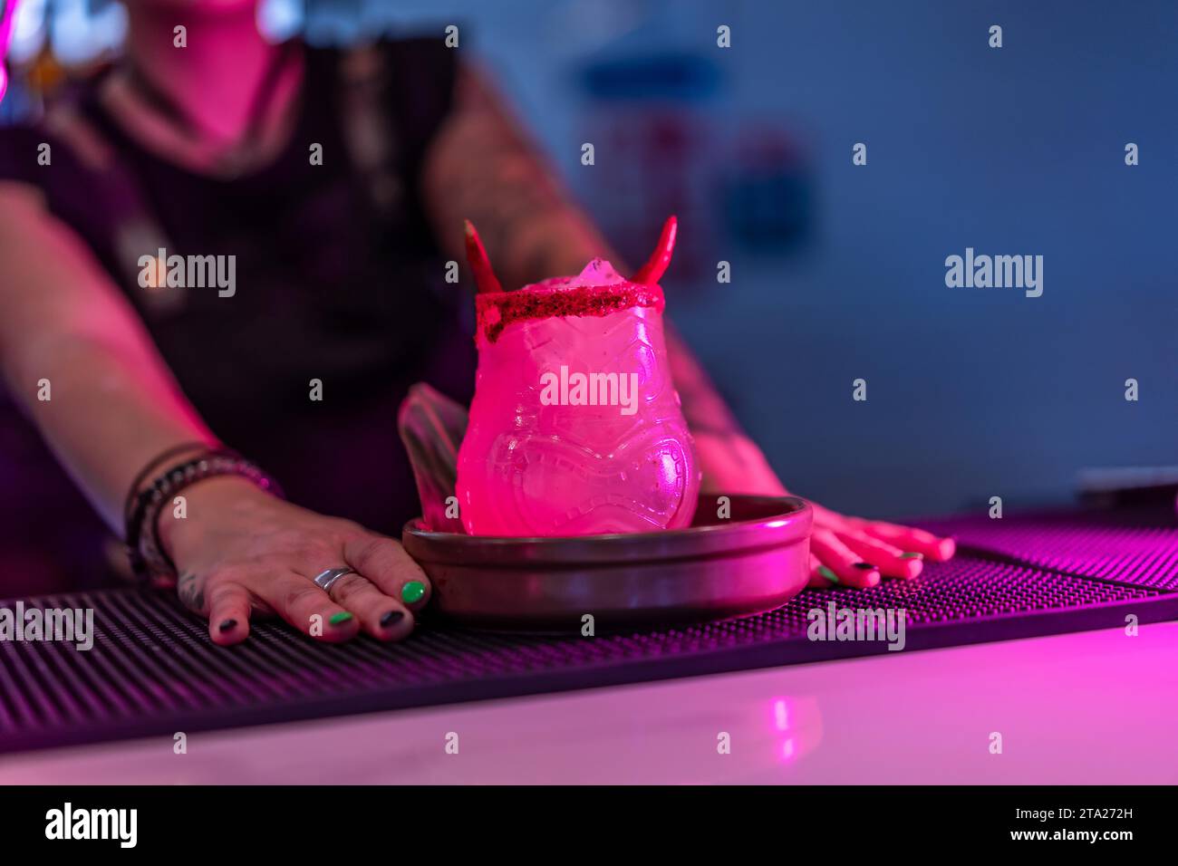 Bartender presenting a margarita cocktail decorated by devil horns in the counter of a night bar with neon lights Stock Photo