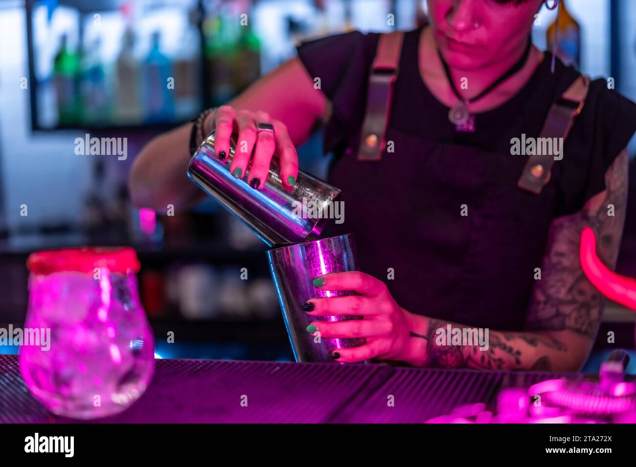 Close-up with focus on a female waiter mixing ingredient preparing a cocktail in the counter of a bar at night Stock Photo