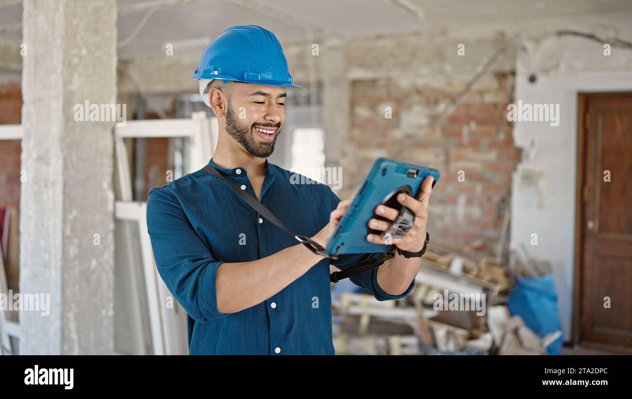Young hispanic man architect wearing hardhat smiling using tablet at construction site Stock Photo