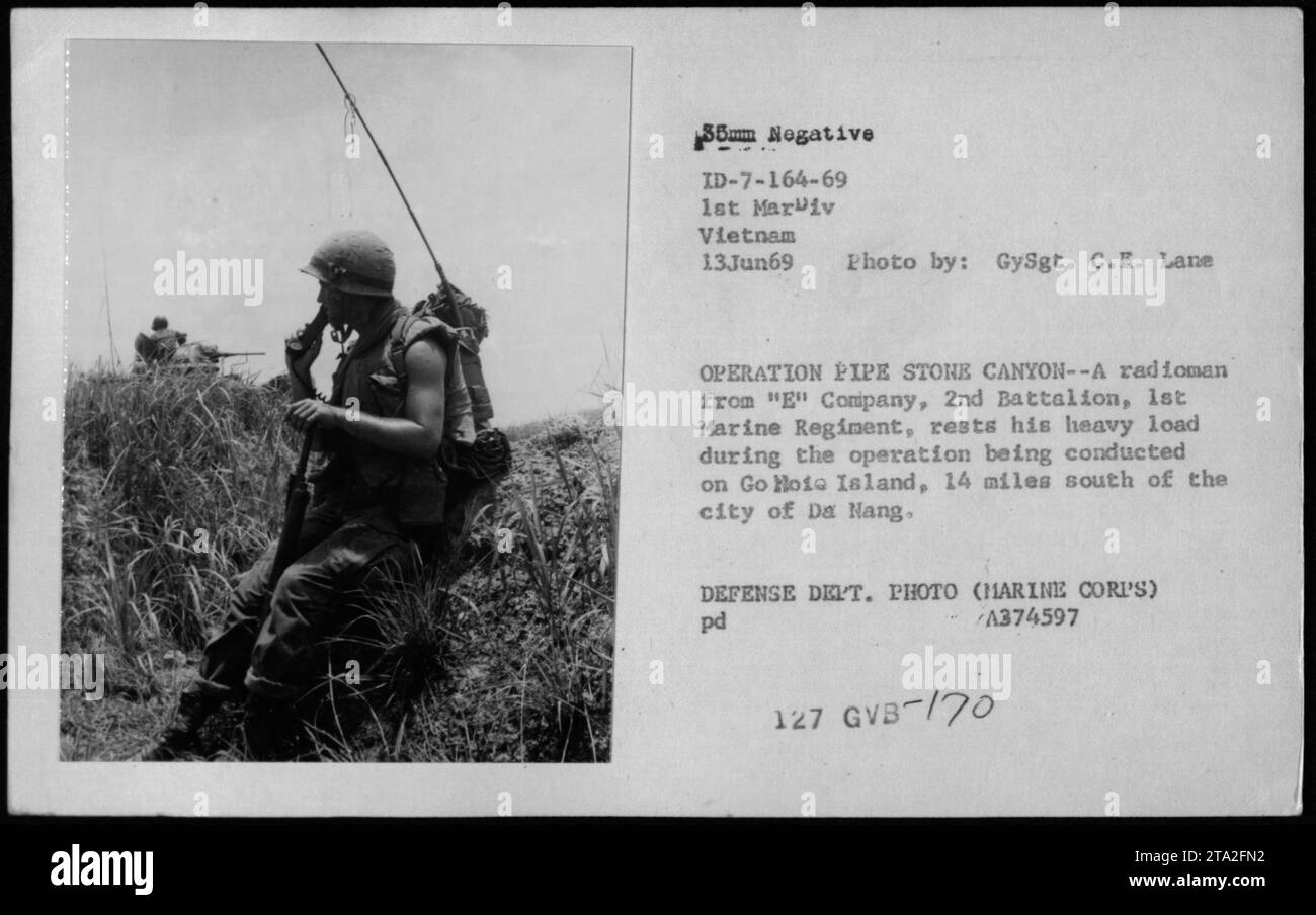 A marine radioman from 'E' Company, 2nd Battalion, 1st Marine Regiment takes a break during Operation Pipe Stone Canyon on Go Hoia Island, located 14 miles south of Da Nang, on June 13, 1969. The image showcases a marine carrying heavy equipment while engaged in military communications. Stock Photo