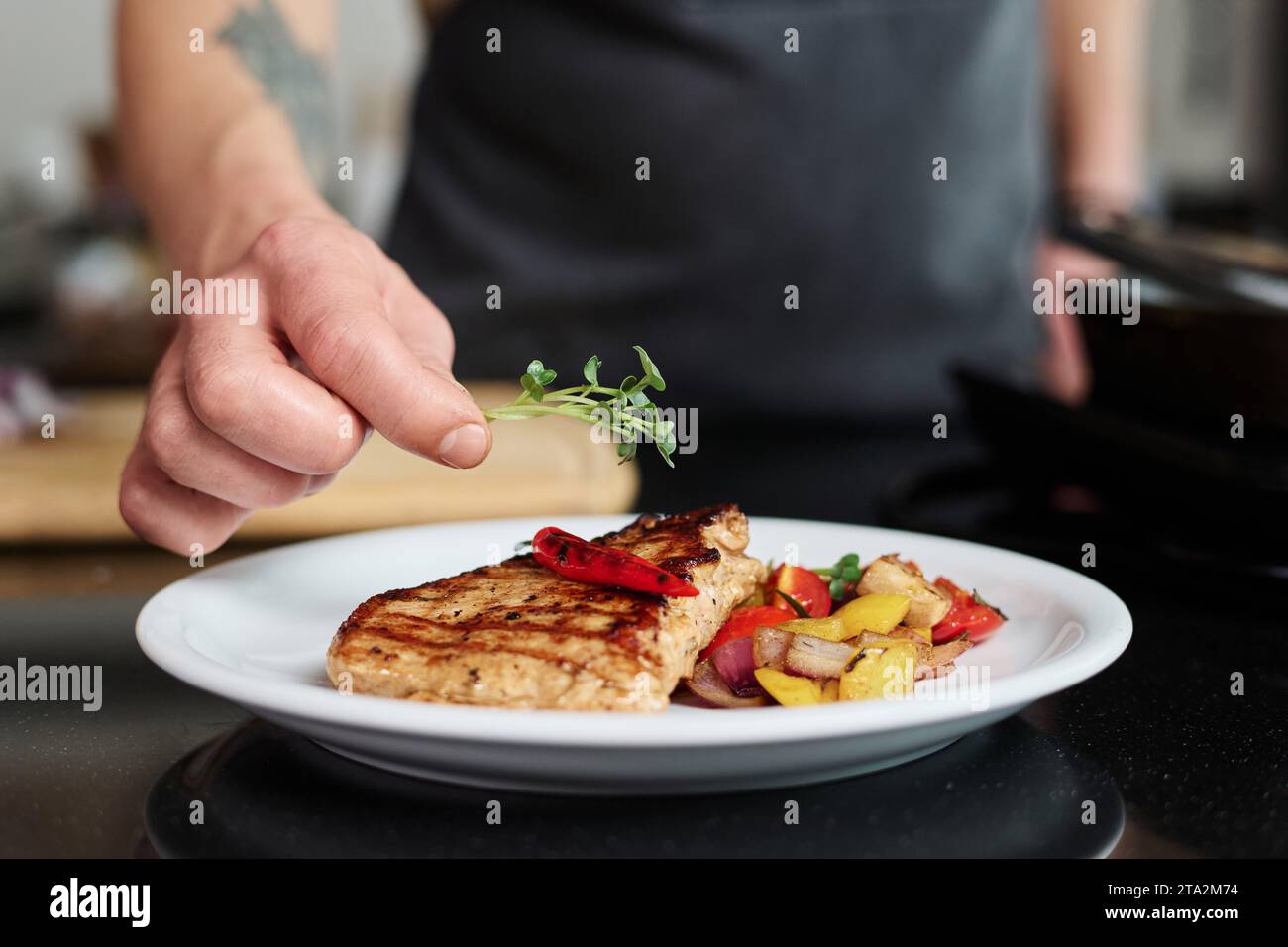 Closeup of hand of unrecognizable man putting green on top of freshly cooked steak with vegetables around, copy space Stock Photo