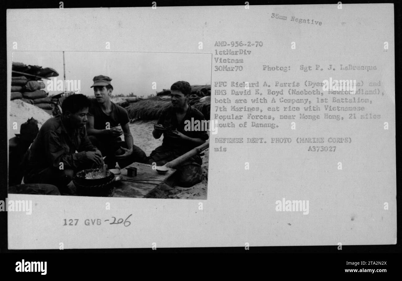 US Marines PFC Richard A. Parris and HM3 David E. Boyd, assigned to A Company, 1st Battalion, 7th Marines, are pictured eating rice with Vietnamese Popular Forces near Monge Hong, located 21 miles south of Danang in Vietnam. The photograph was taken on March 30, 1970 by Sgt P. J. Labrecque and is part of the Defense Department's collection (HARINE CORPS). Stock Photo