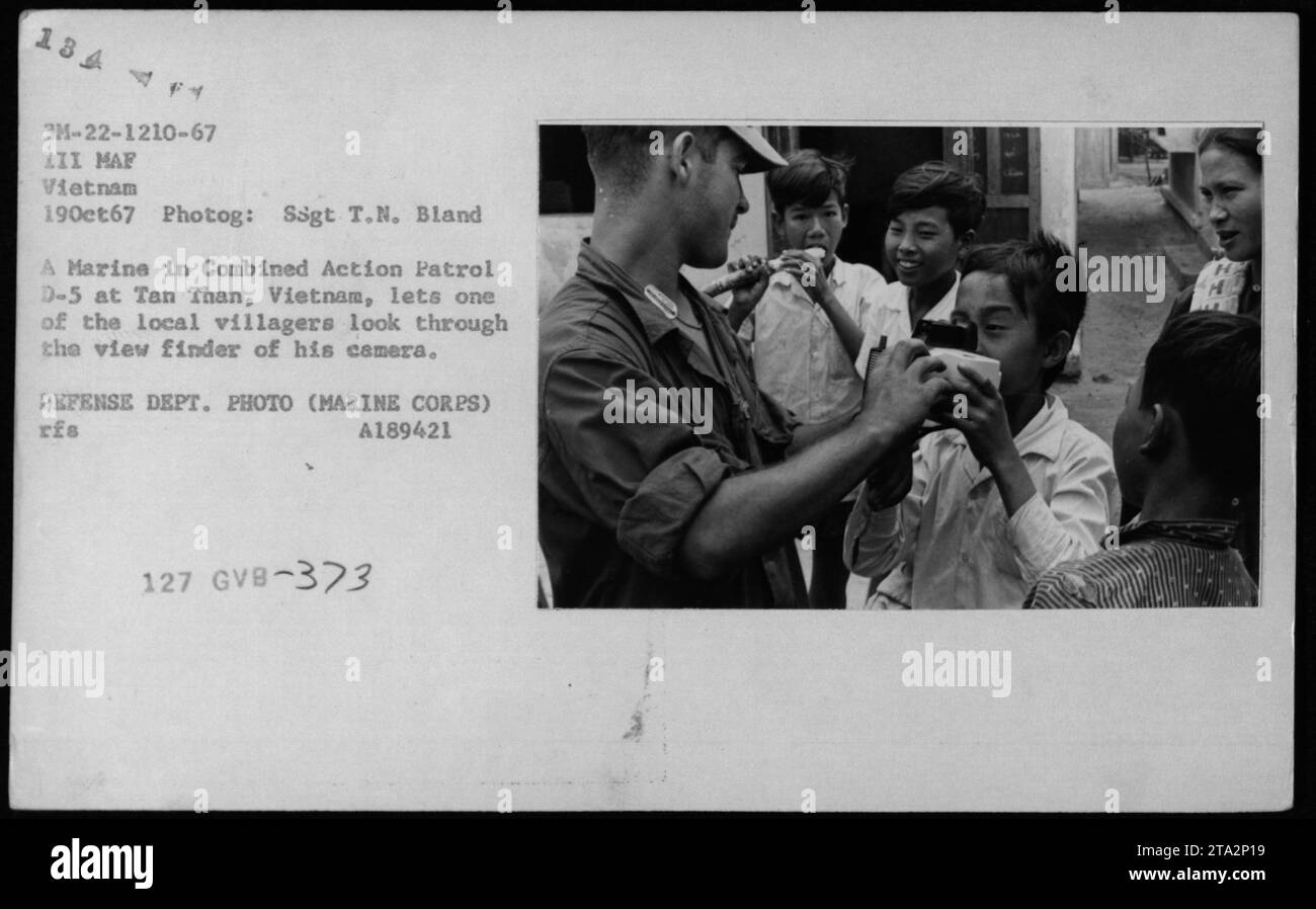 A Marine in a Combined Action Patrol D-5 at Tan Than, Vietnam, allowing a local villager to peer through the viewfinder of his camera. The photograph was taken on October 19, 1967, by Staff Sergeant T.N. Bland, as part of a series capturing Vietnamese civilian life during the Vietnam War. This image was released by the Defense Department and belongs to the Marine Corps. Stock Photo