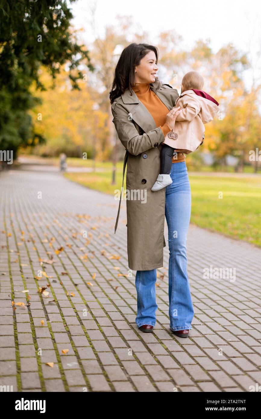 Young woman holding a cute baby girl in the autumn park Stock Photo