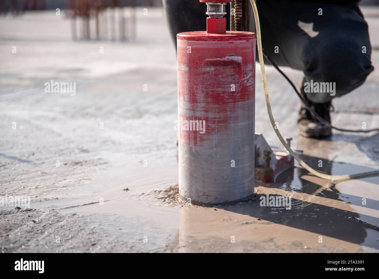 A worker drills a reinforced concrete floor using a drilling rig with a