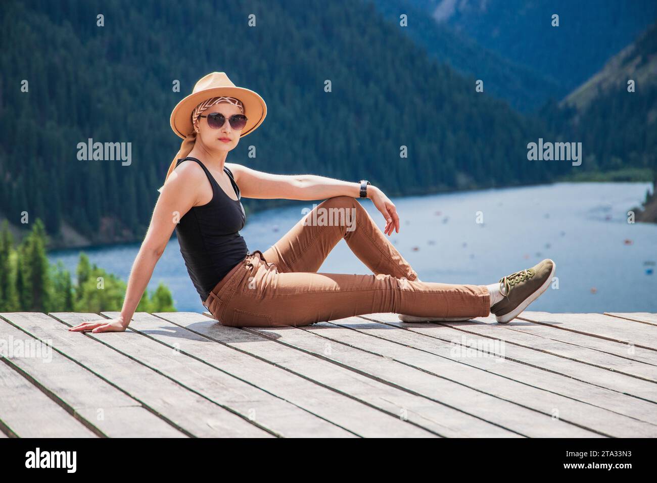 A young woman in safari style went out to nature outside the city, taking a weekend tour to the Kolsai mountain lake in the Tien Shan mountains Stock Photo