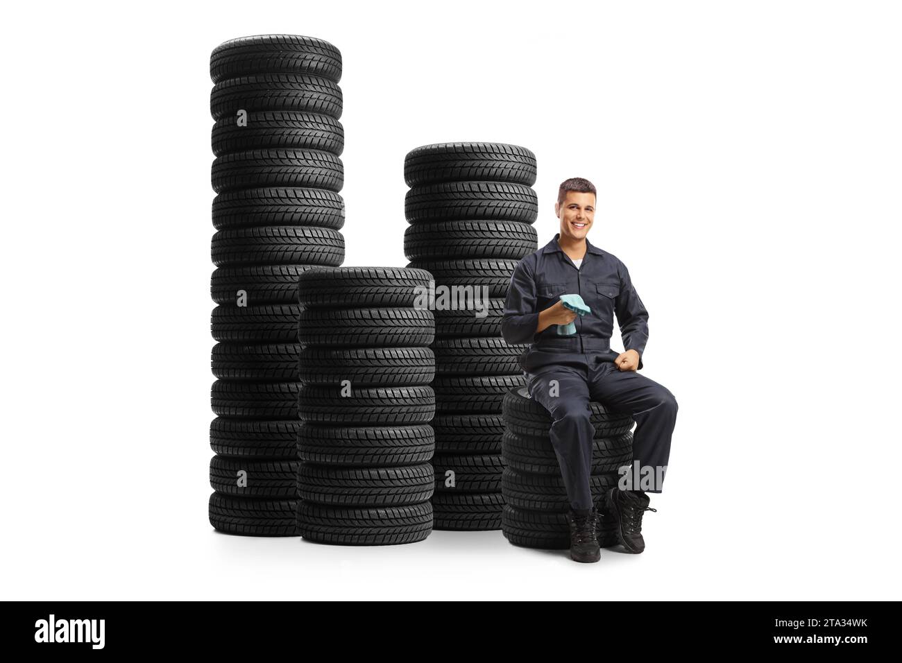 Auto mechanic smiling and sitting with piles of tires isolated on white background Stock Photo