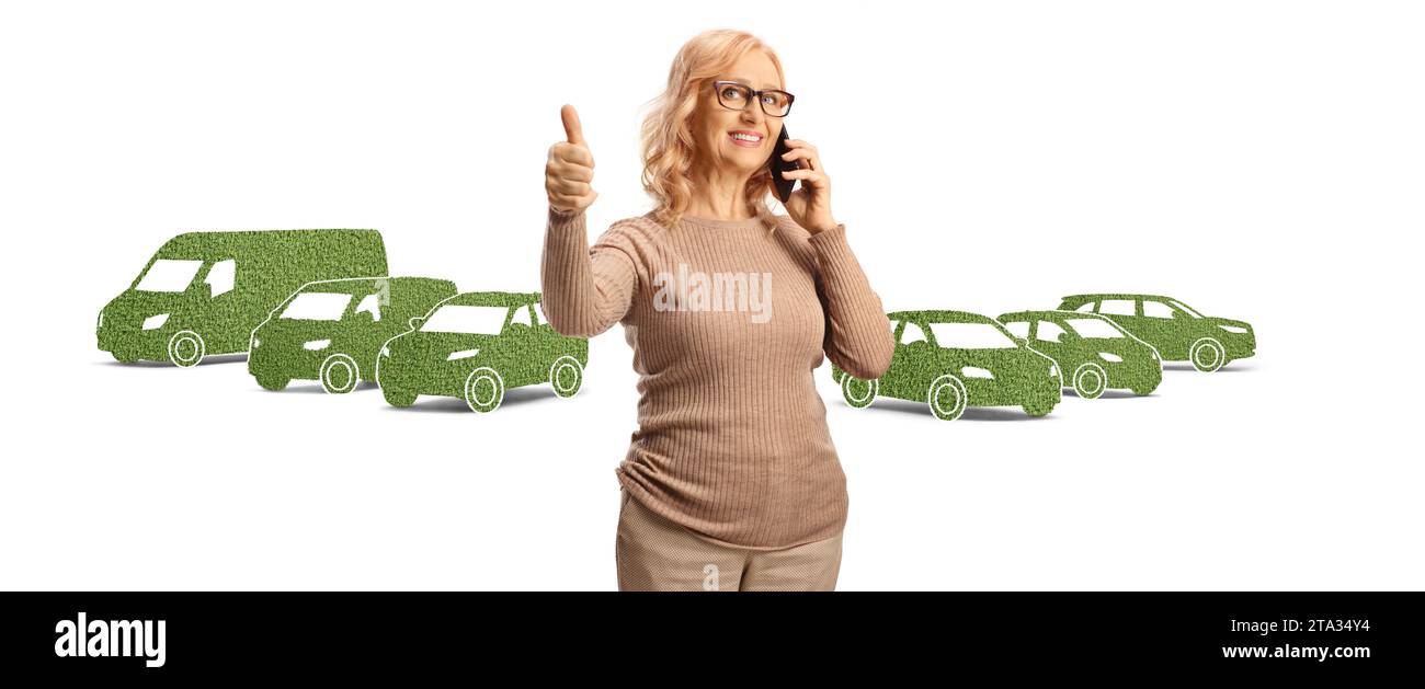 Mature woman making a phone call and gesturing thumbs up in front of green electric vehicles isolated on white background Stock Photo