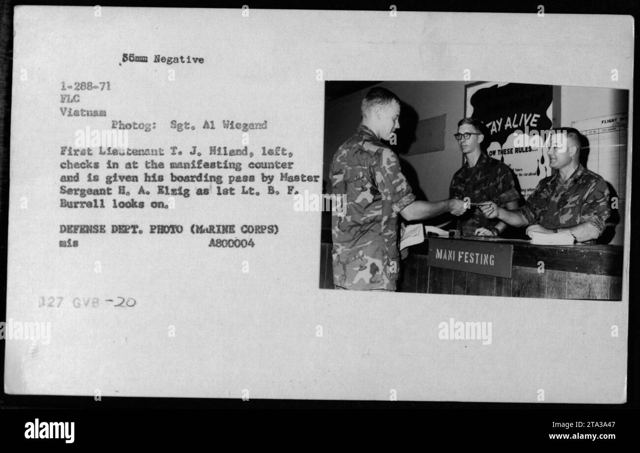 First Lieutenant T.J. Hiland checks in at the manifesting counter in Vietnam, receiving his boarding pass from Master Sergeant H.A. Elzig. First Lieutenant B.F. Burrell observes the process. This photograph captures the administrative and clerical activities of American Military personnel during the Vietnam War. ğ Stock Photo