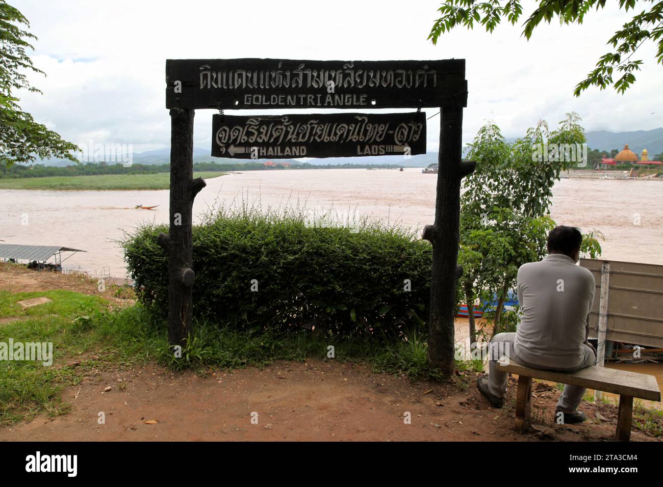Chiang Saen, Thailand - August 04 2012: Old Thai sat next to a sign at the Golden Triangle indicating the directions of the Thai and Laos borders. On Stock Photo
