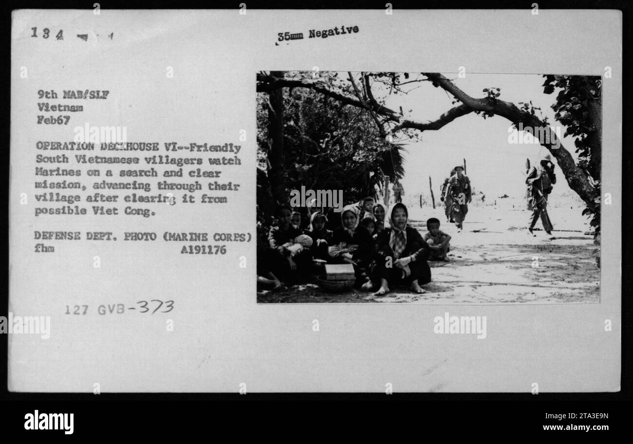 Vietnamese civilians observe Marines conducting a search and clear mission in their village as part of Operation DECKHOUSE VI in February 1967. The Marines are advancing through the village after successfully clearing it of any potential Viet Cong presence. This photograph is a Department of Defense image taken by the Marine Corps. Stock Photo