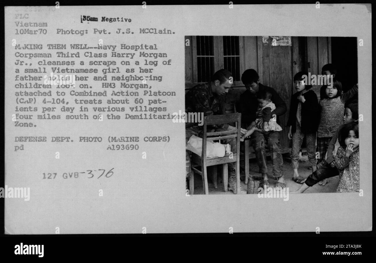 Navy Hospital Corpsman Third Class Harry Morgan Jr. is shown cleansing a scrape on the leg of a small Vietnamese girl, while her father holds her and nearby children watch. HM3 Morgan, of Combined Action Platoon (CAP) 4-104, attends around 60 patients daily in villages located four miles south of the Demilitarized Zone (DMZ). This photograph was taken on March 10, 1970, in FLC, Vietnam, during the Vietnam War. Stock Photo