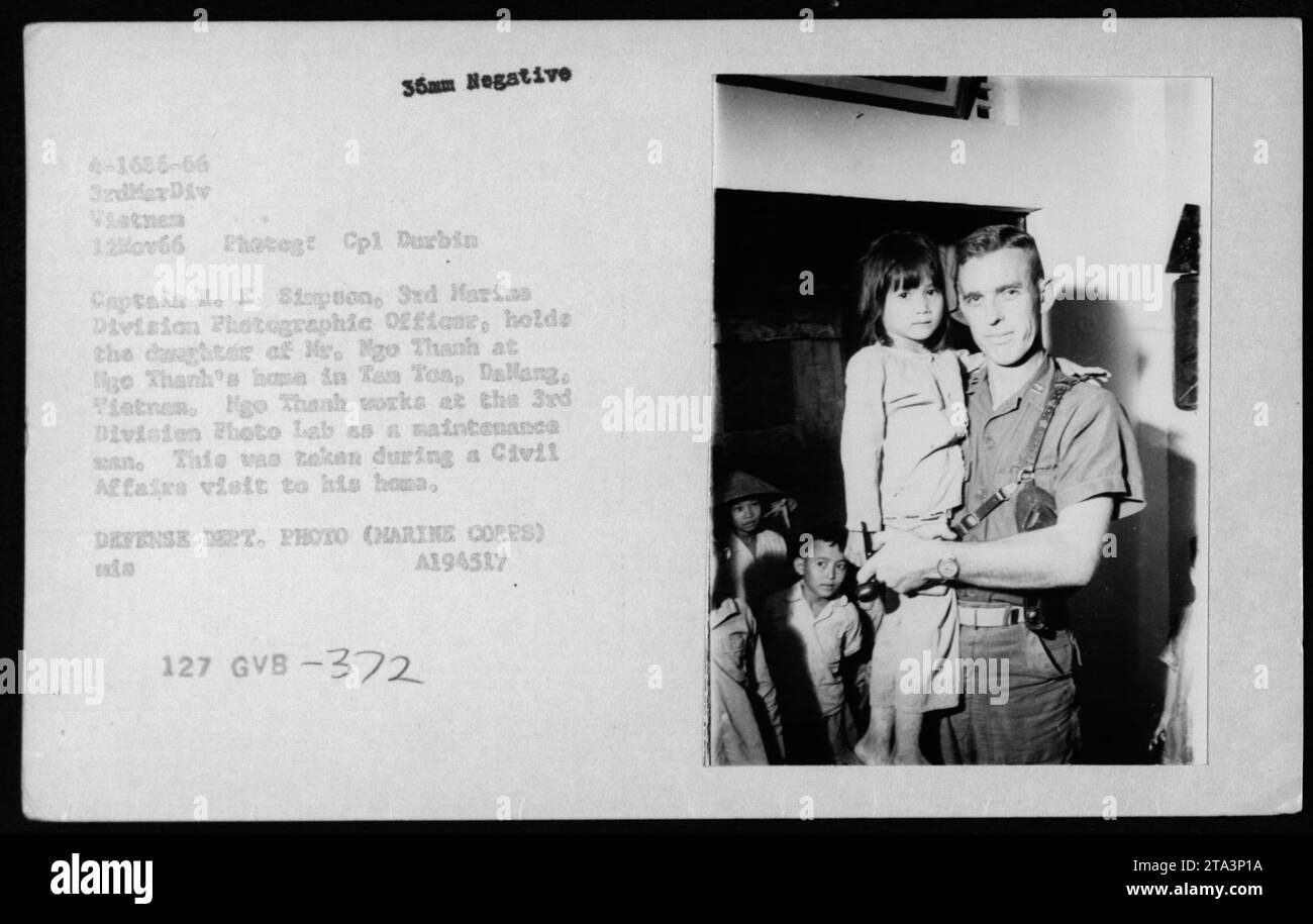 'Captain B.E. Simpson, 3rd Marine Division Photographic Officer, holding the daughter of Mr. Ngo Thanh during a Civil Affairs visit to Tan Toa, Dallang, Vietnam. Mr. Thanh works at the 3rd Division Photo Lab as a maintenance staff. This photo was taken on November 12, 1966, illustrating the interaction between American military personnel and Vietnamese civilians during the Vietnam War.' Stock Photo