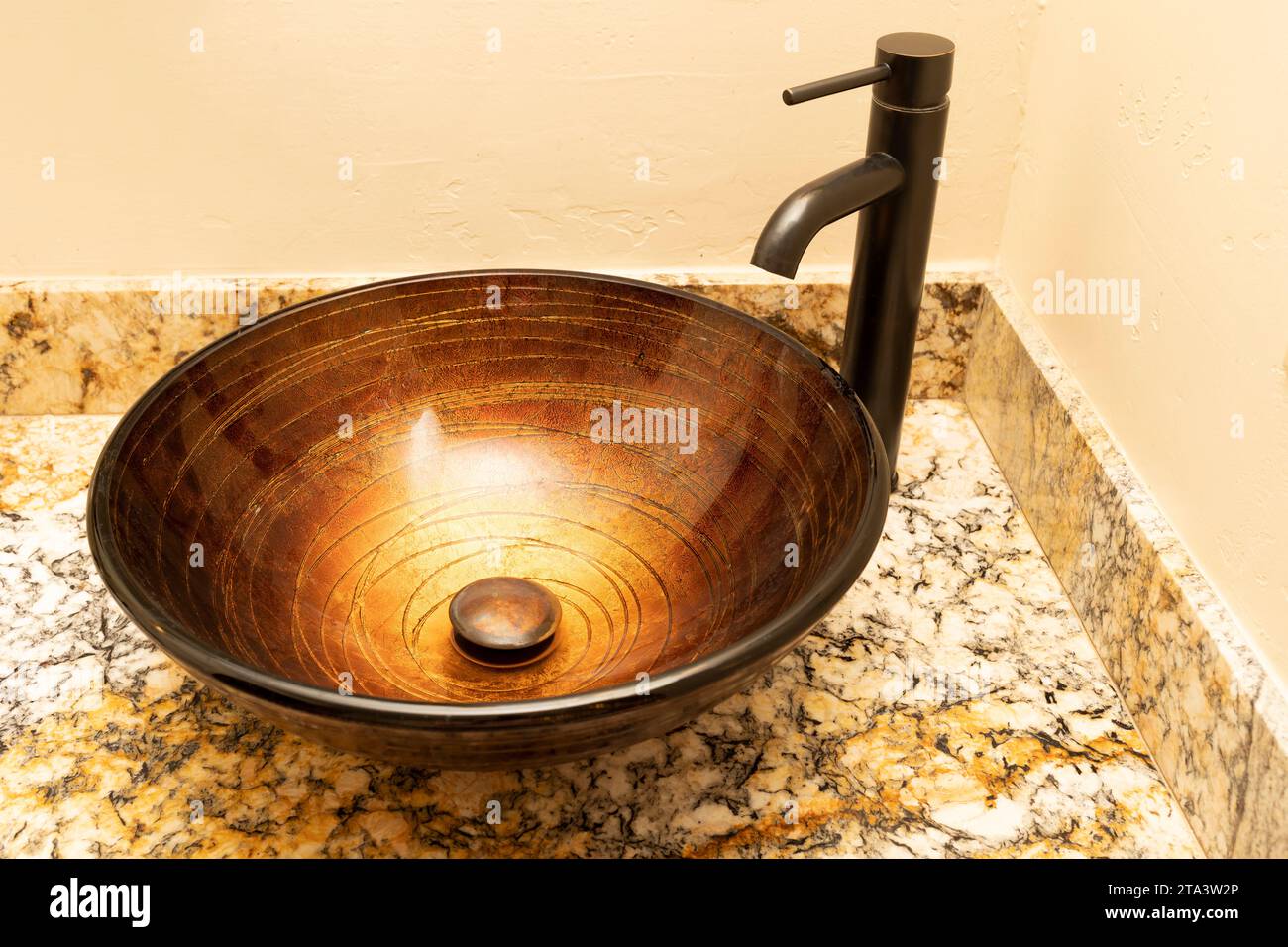 Golden Greek Glass Bowl Vessel Bathroom Sink And Faucet Set In Antique Rubbed Bronze Finish On Granite Countertop, Beige Walls. Close Up Bath Fixture Stock Photo