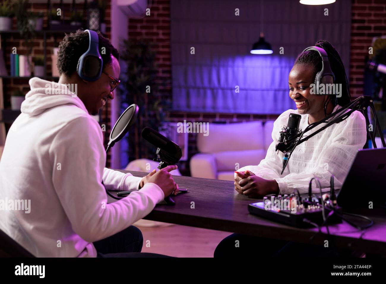 Online show host interviewing guest sharing funny anecdotes and jokes during live broadcast. Talking show interviewer using professional microphone and camera to record podcast Stock Photo