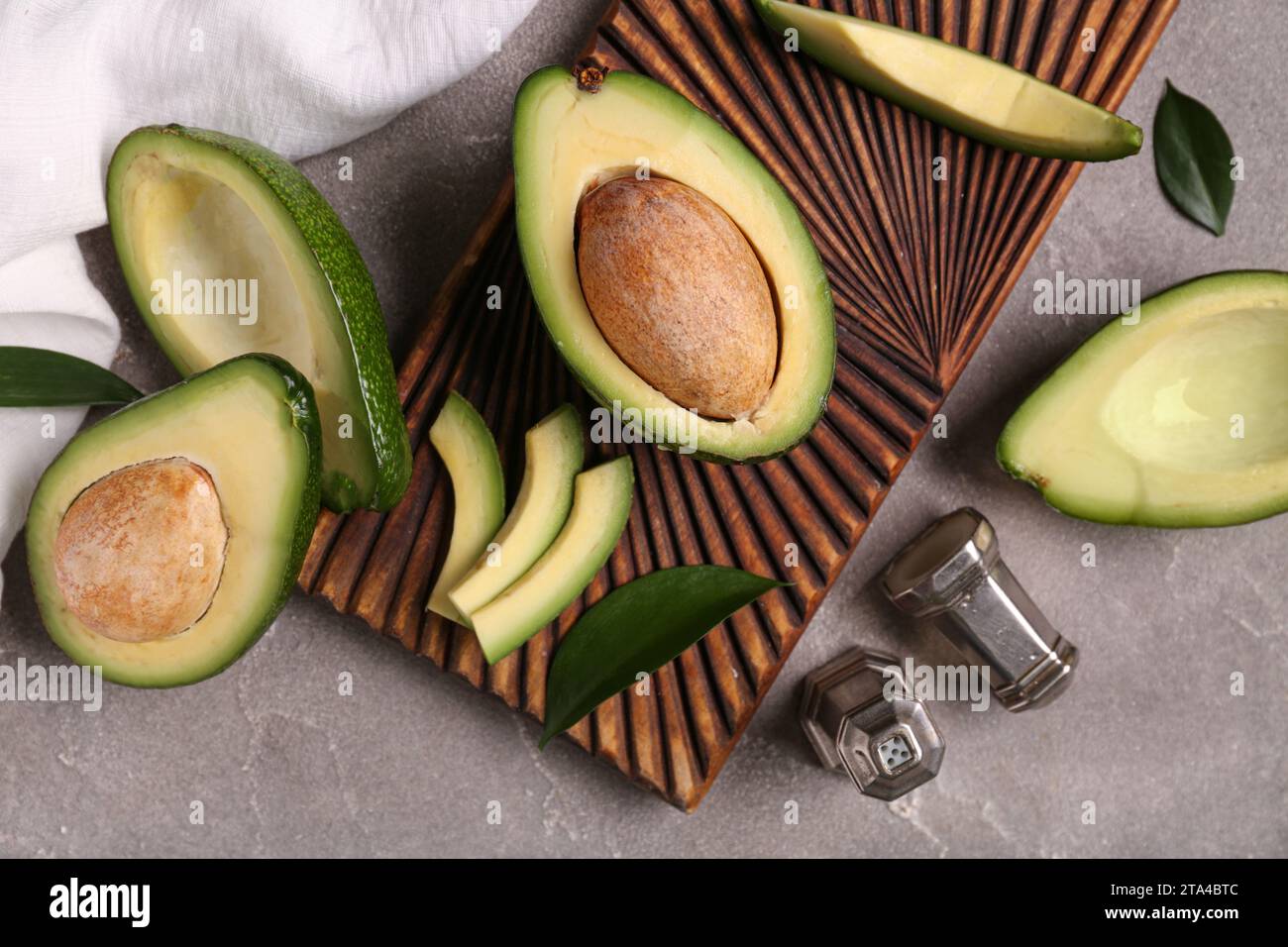 Wooden board with cut fresh avocados and leaves on grey background ...