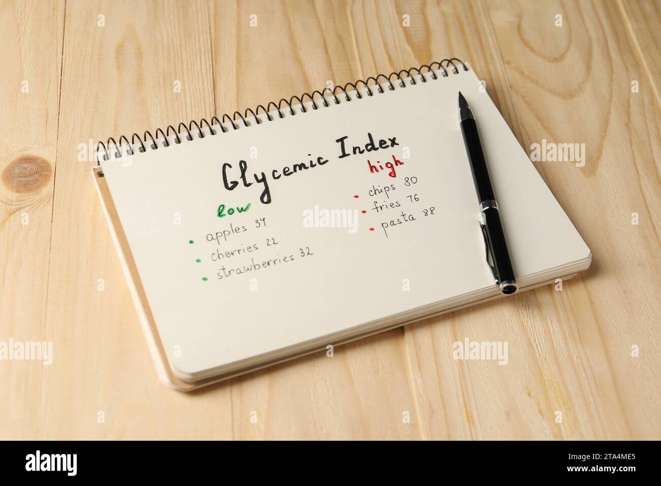 List with products of low and high glycemic index in notebook and pen on wooden table Stock Photo