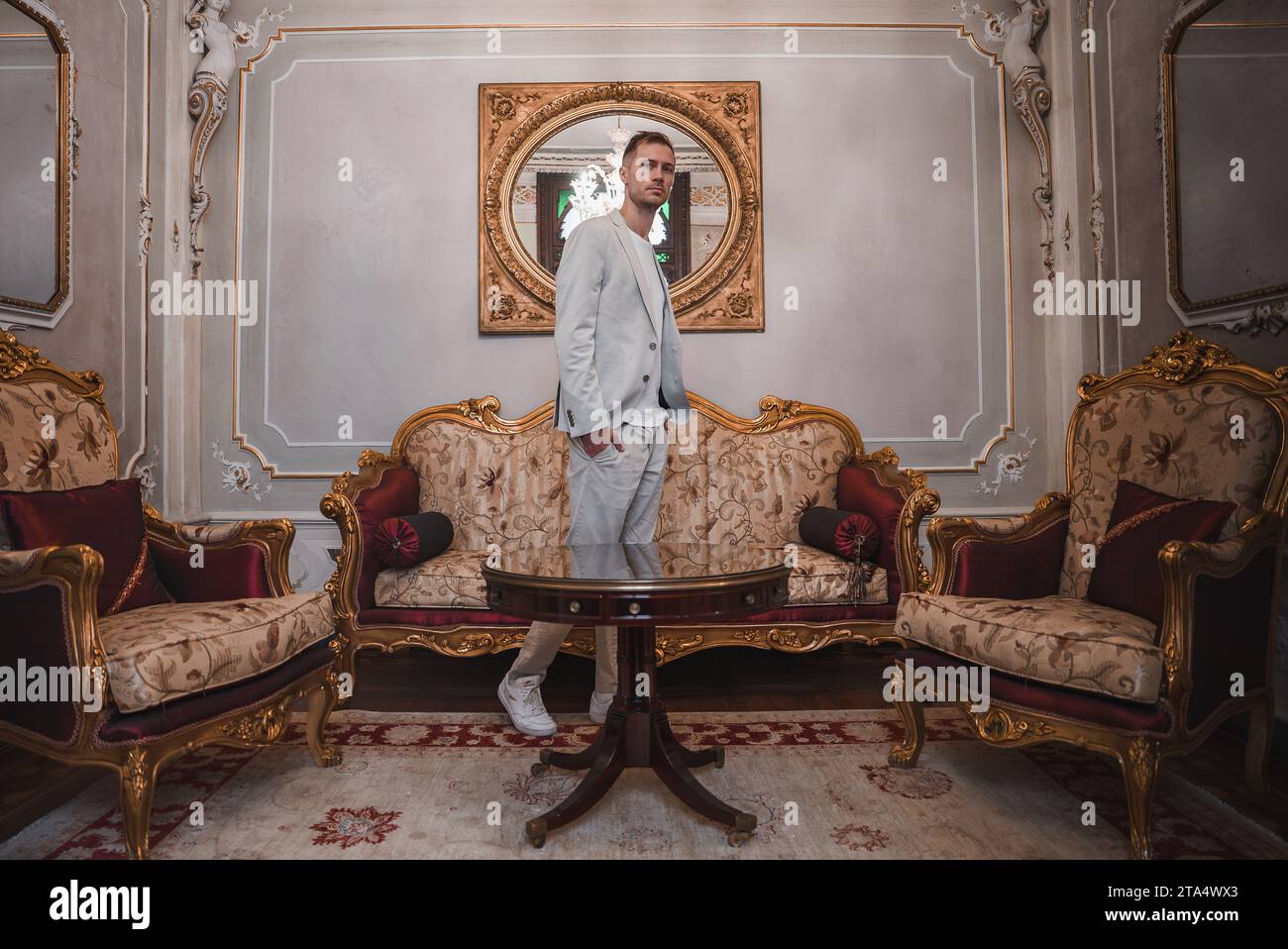 Elegant man in suit standing on luxurious Venetian-style couch in ornate room. Stock Photo