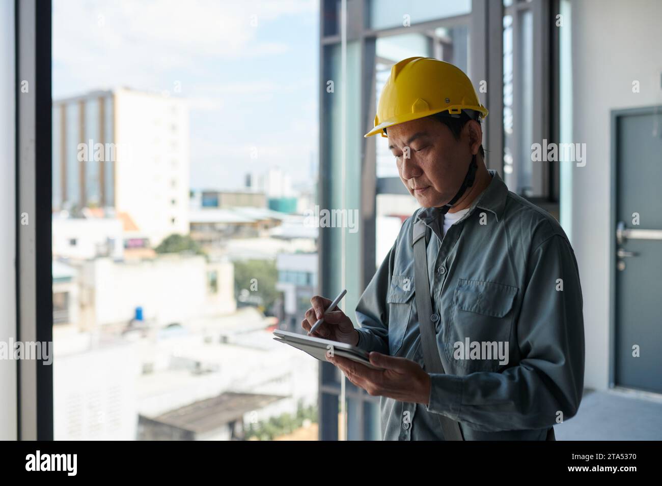 Contractor wearing hardhat when working at construction site, filling form on tablet computer Stock Photo
