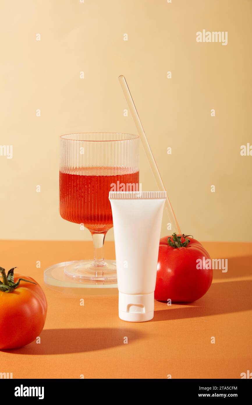 Front view of an unlabeled cosmetic tube and a glass of tomato juice on