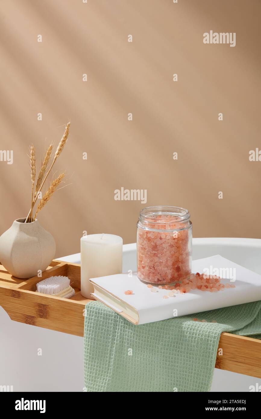 Wooden bathtub tray with a flower pot, foot brush, candle, book and a jar pink himalayan salt placed on. Pink himalayan salt blast away dead cells for Stock Photo