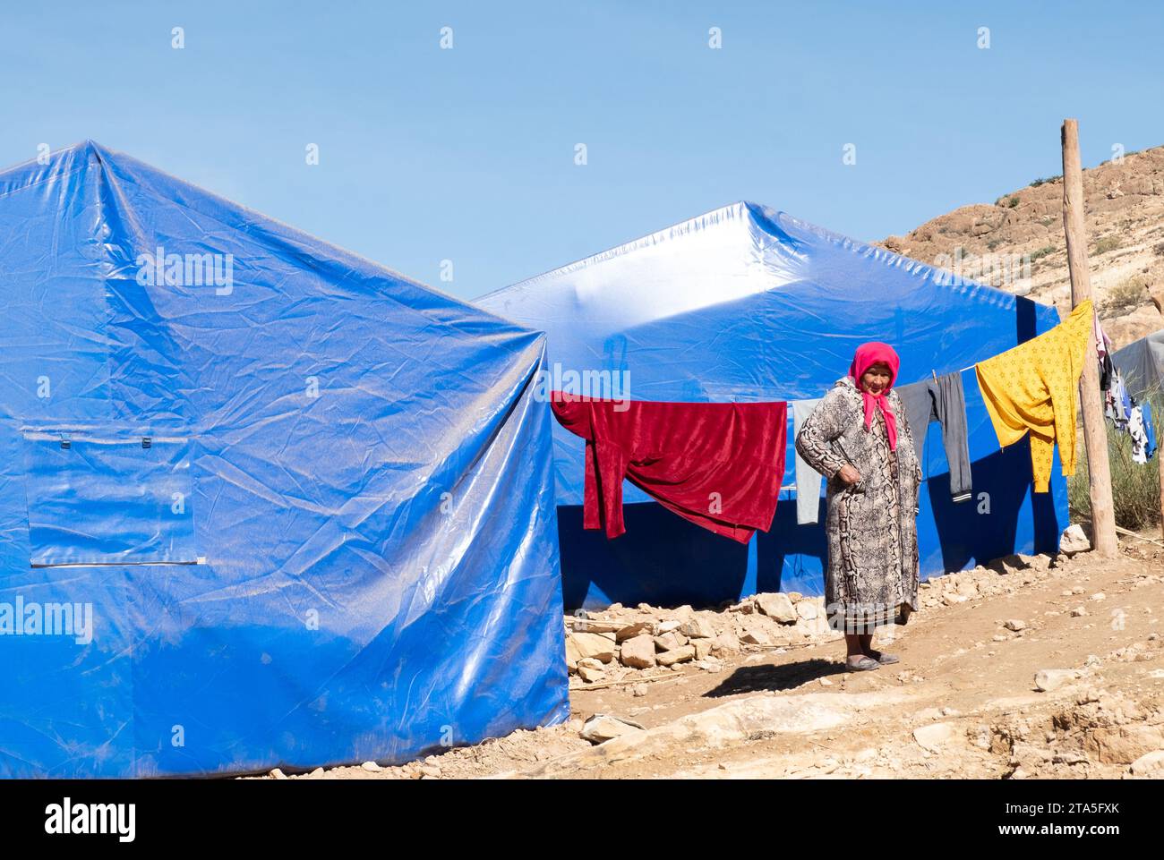 Woman stands outside blue relief tents, Sidi Hssain, Atlas Mountains, Morocco Stock Photo