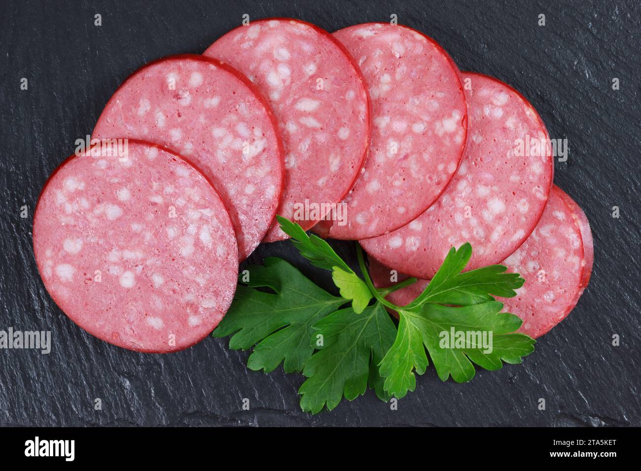Pork Meat Smoked Sausage Cervelat Sliced With Parsley Leaf On Shale Stone Plate, Top View Flat Layout Stock Photo