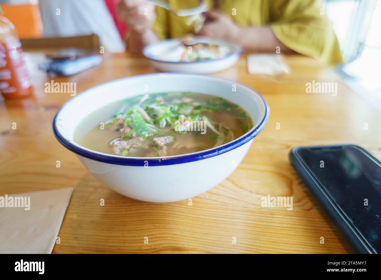 Vietnamese Pho dish on the table. Unrecognizable people enjoying lunch in a restaurant. Stock Photo