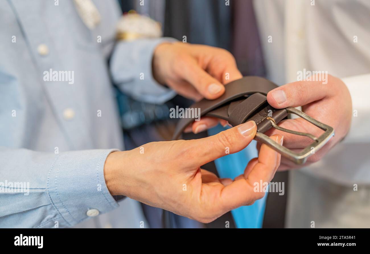 Close-up of hands holding a black leather belt with a silver buckle in a wedding store Stock Photo