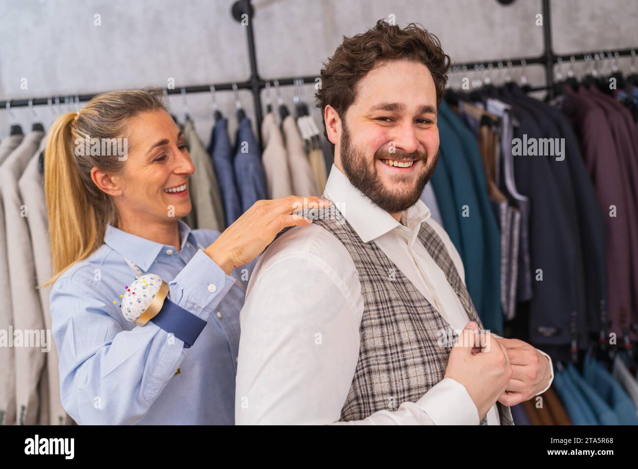 Tailor fitting a vest on a cheerful male client in a clothing store