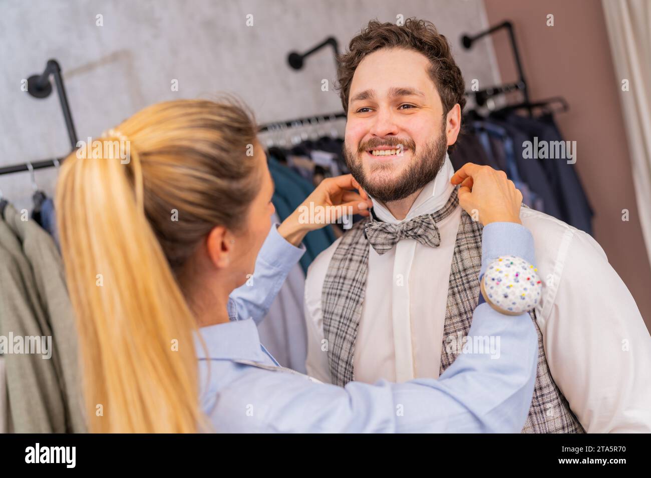 Tailor fitting a bow tie on a cheerful man in a fashion store with