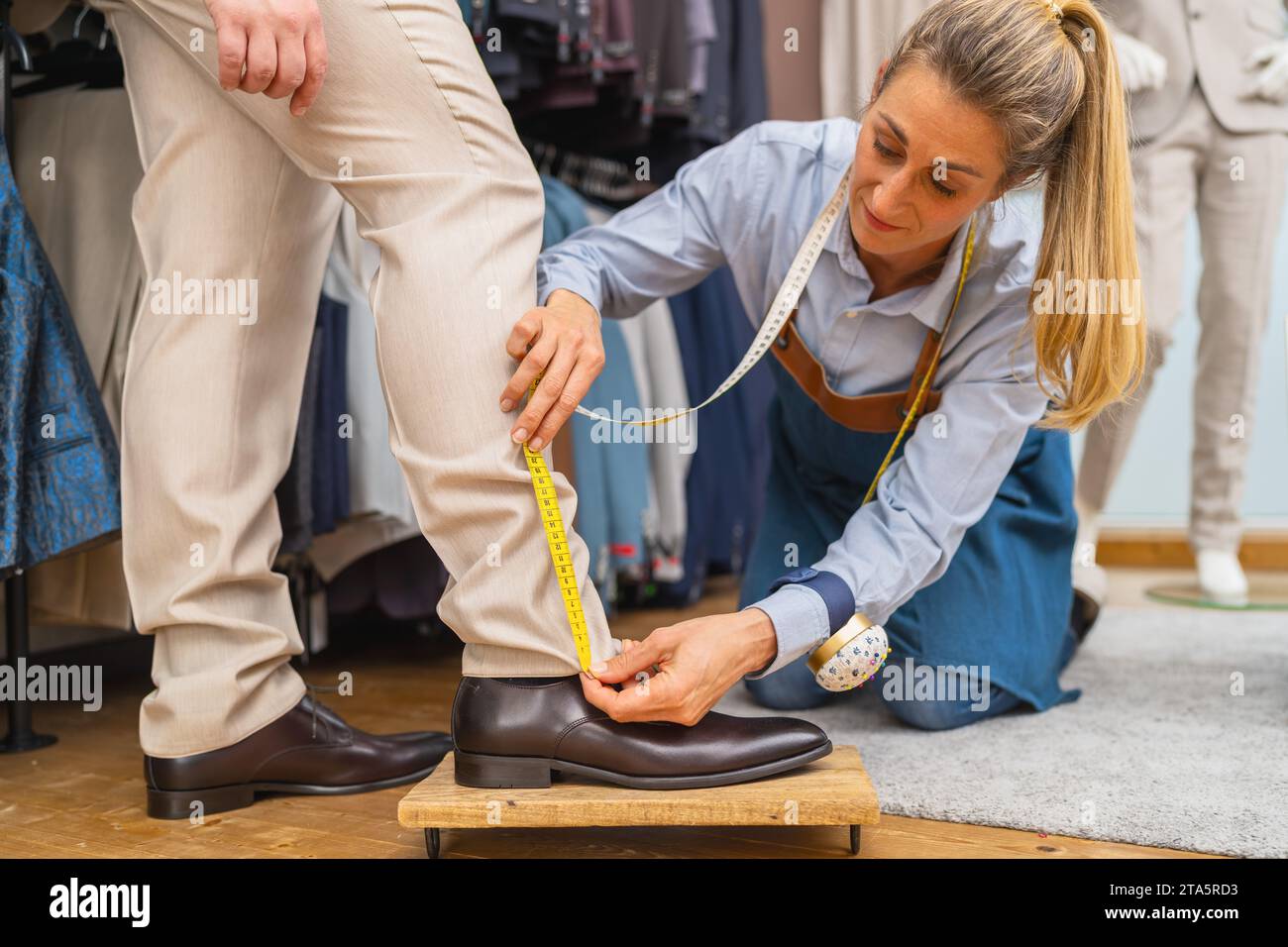 https://c8.alamy.com/comp/2TA5RD3/tailor-measures-mans-trouser-length-with-yellow-tape-at-shoe-level-at-a-wedding-store-2TA5RD3.jpg