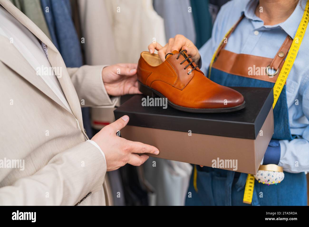 man holding a tan dress shoe above a shoe box with a tailor holding a tape measure Stock Photo