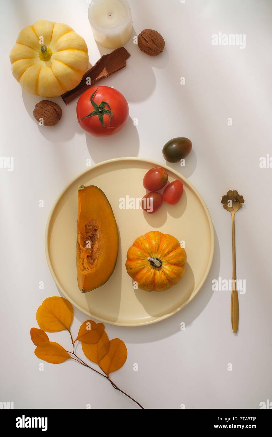 Ideas for party decorations for Thanksgiving. Ceramic plate containing pumpkins, decorated with ripe tomatoes, cinnamon and walnuts on white backgroun Stock Photo