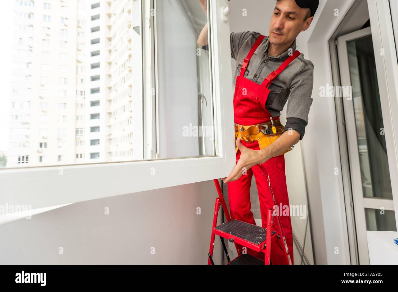 Worker in uniform installing roller window blind indoors Stock Photo