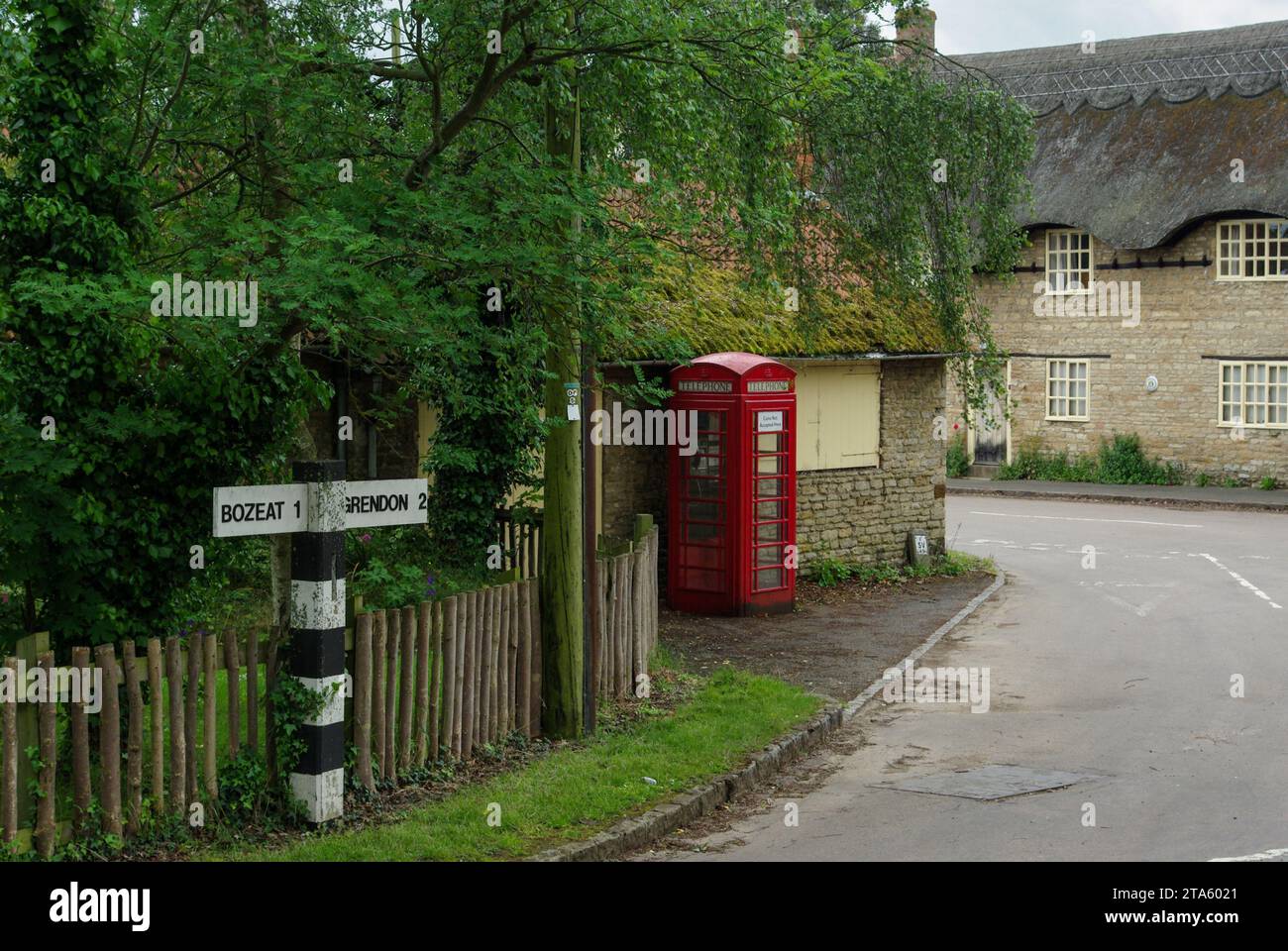 Street scene in the English village of Easton Maudit, Northamptonshire, UK; with black and white road sign, red telephone box and thatched cottage Stock Photo