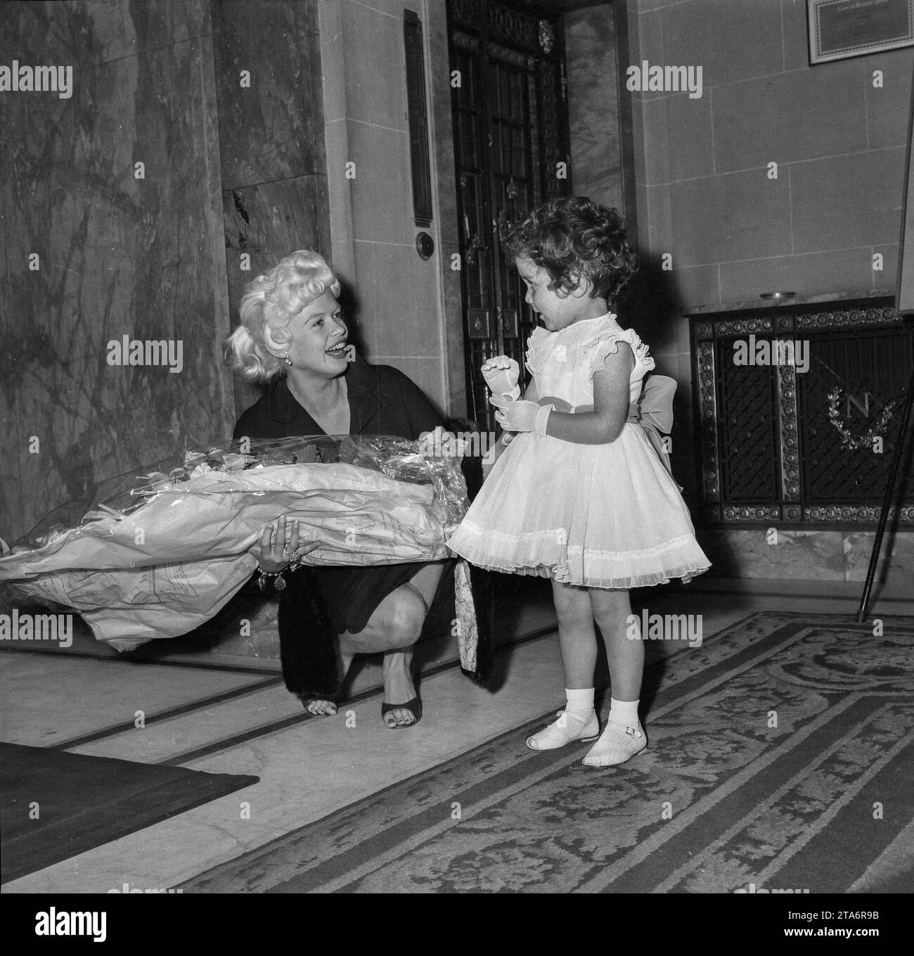 Jayne Mansfield accepts flowers from a little girl while she judges the Miss Soho beauty contest of 1958 Stock Photo