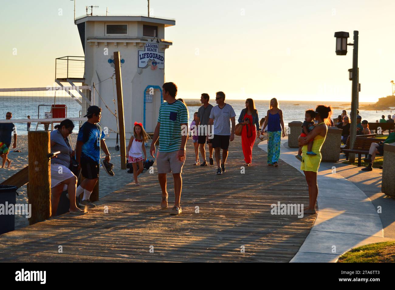 A large crowd walks along the boardwalk at sunset with a view of the ocean at Laguna Beach Stock Photo