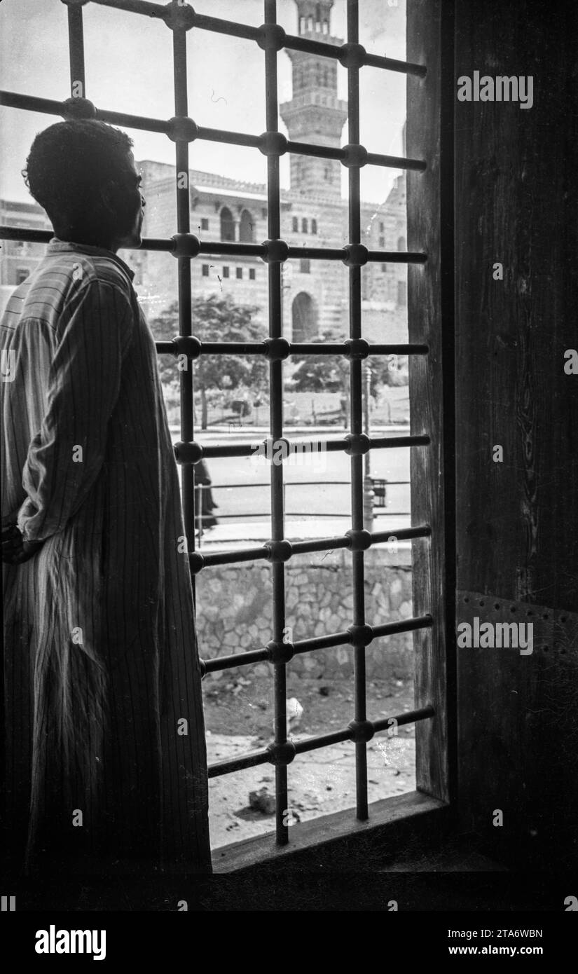 A young man stares out of a window in the Cairo Citadel in Egypt in the 1930s, he is looking towards the Mosque Sultan Hassan Stock Photo